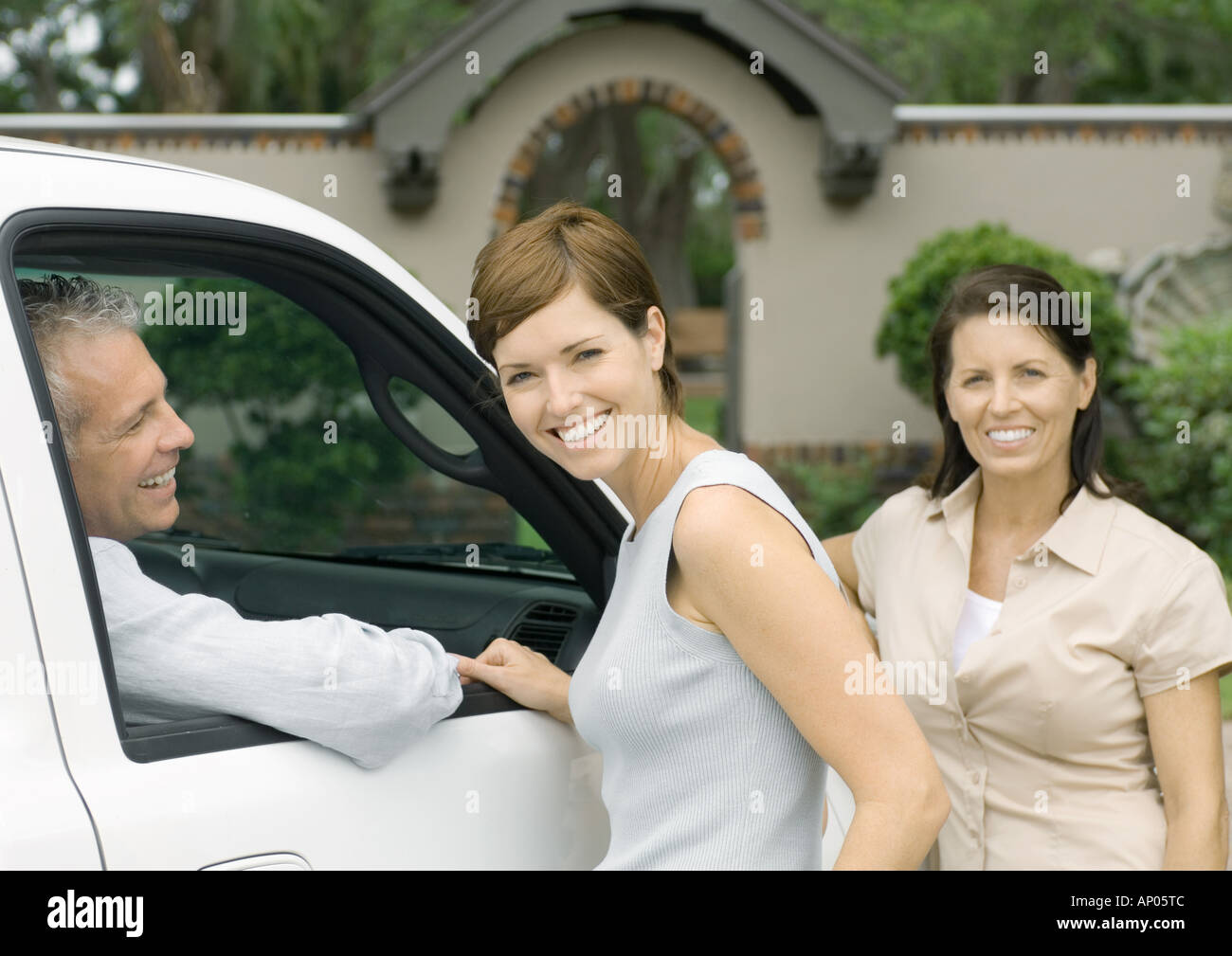 Two women standing next to vehicle with man inside, smiling Stock Photo