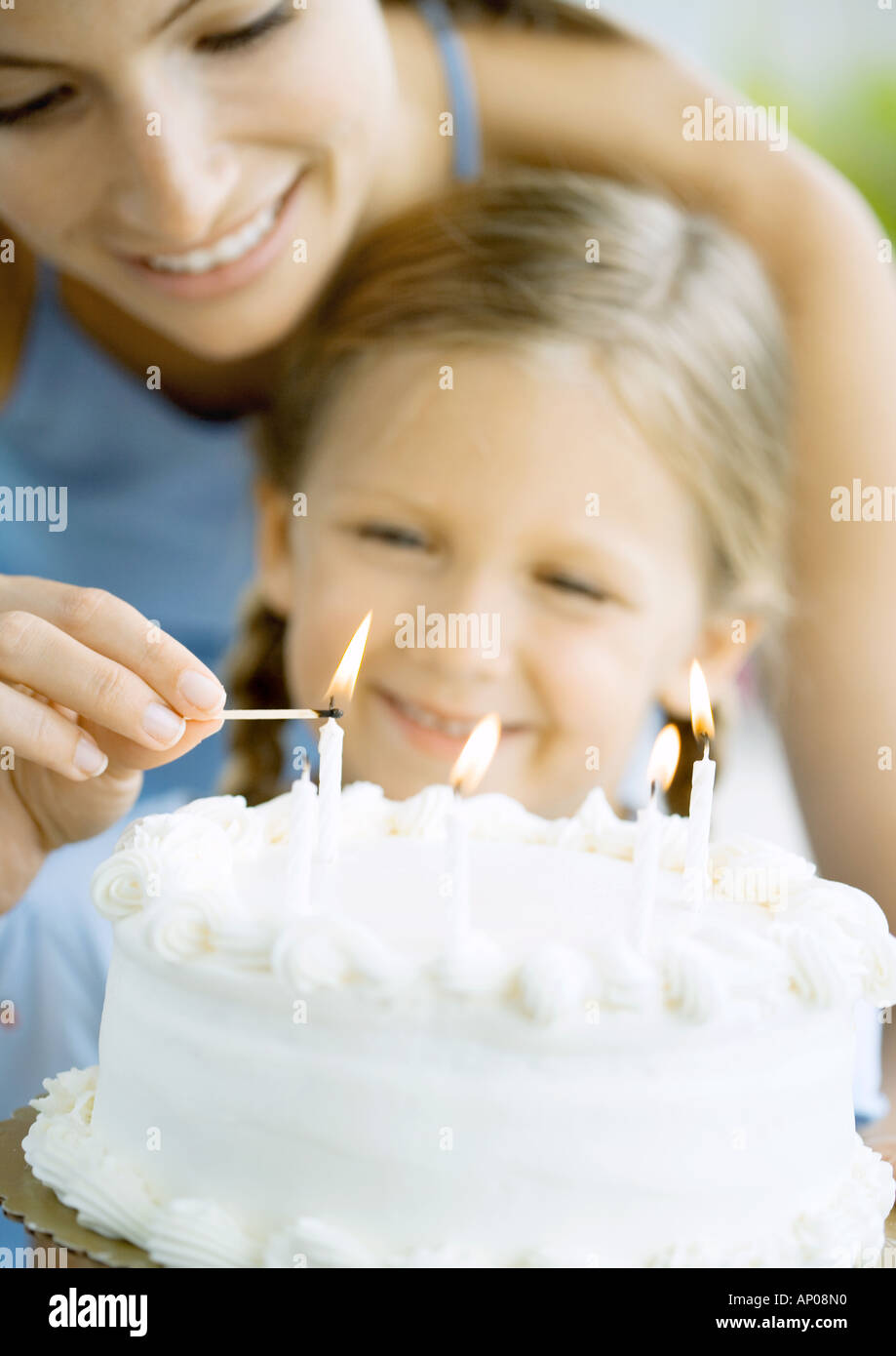mother lighting candles on birthday cake for daughter stock photo
