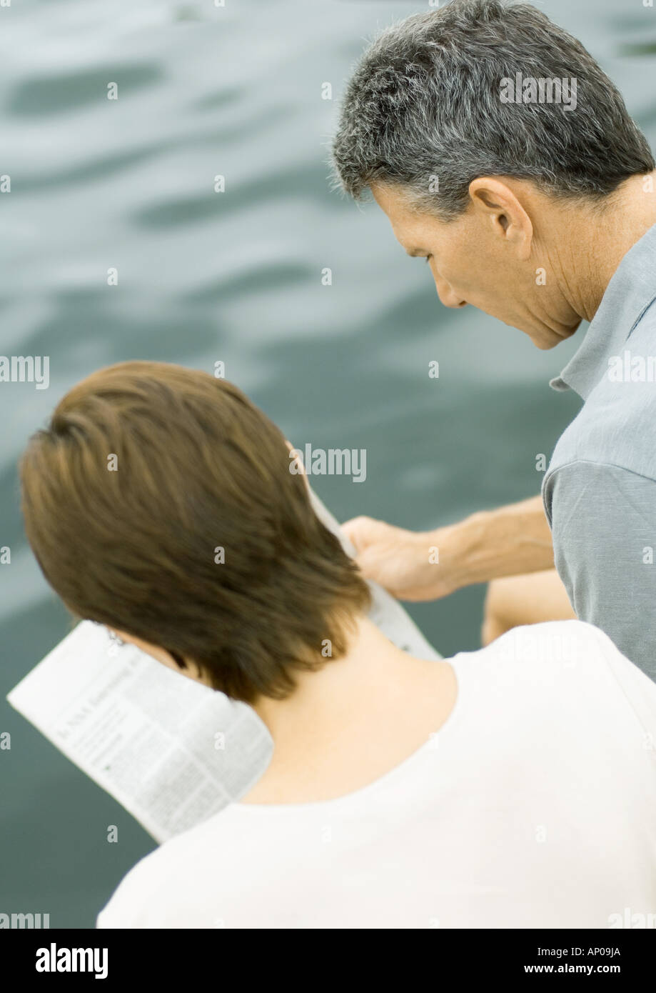 Couple reading newspaper together, water in background Stock Photo