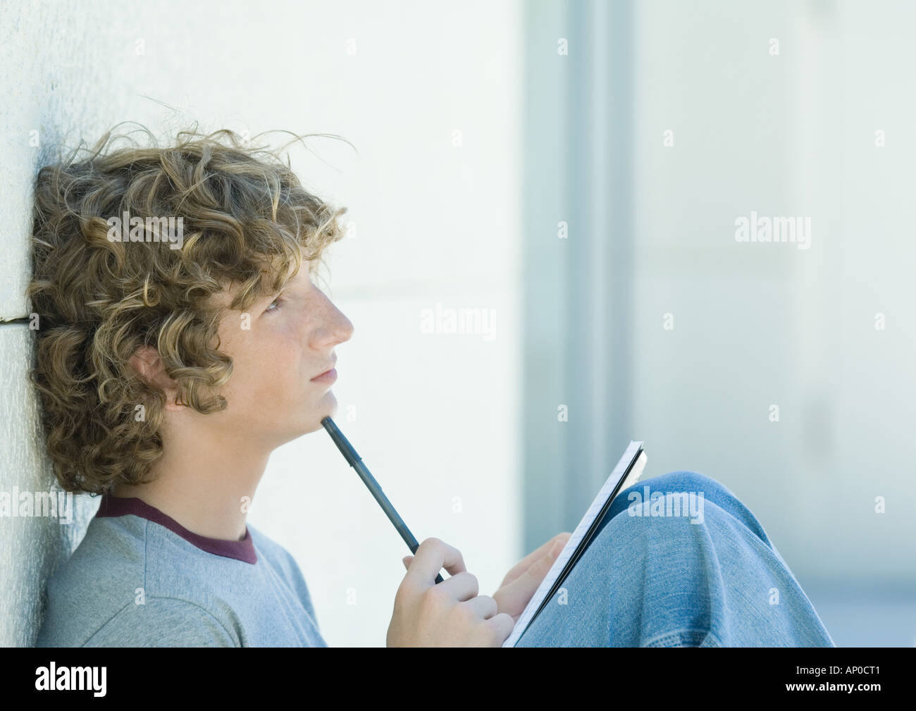Teenage boy sitting with pen and notebook, side view Stock Photo