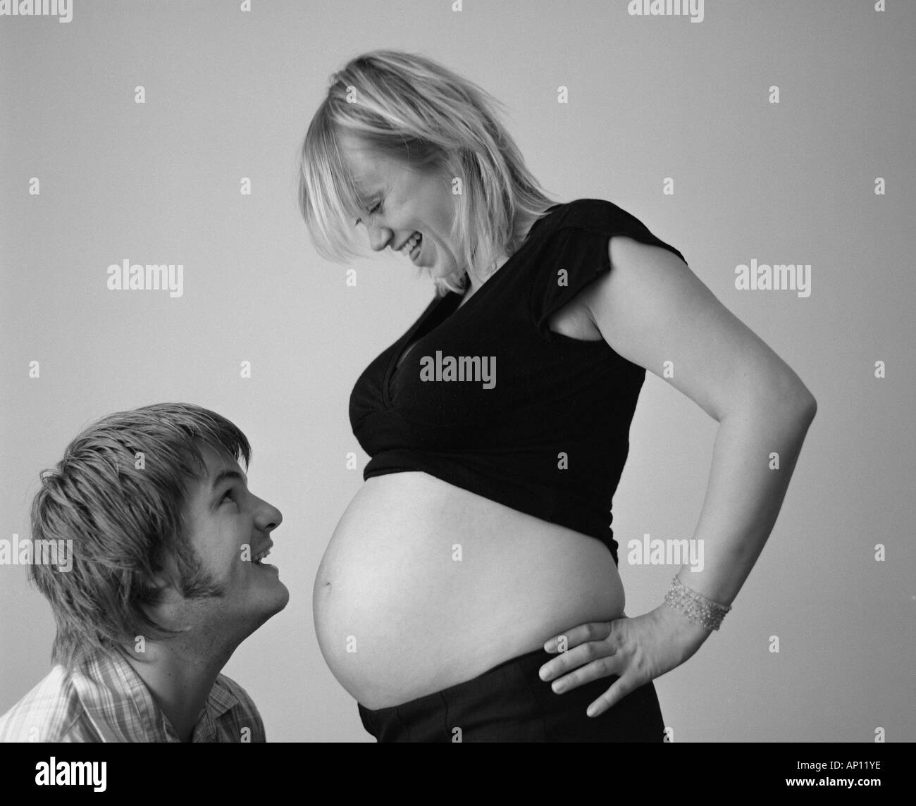 Young couple laughing towards each other and her pregnant belly Stock