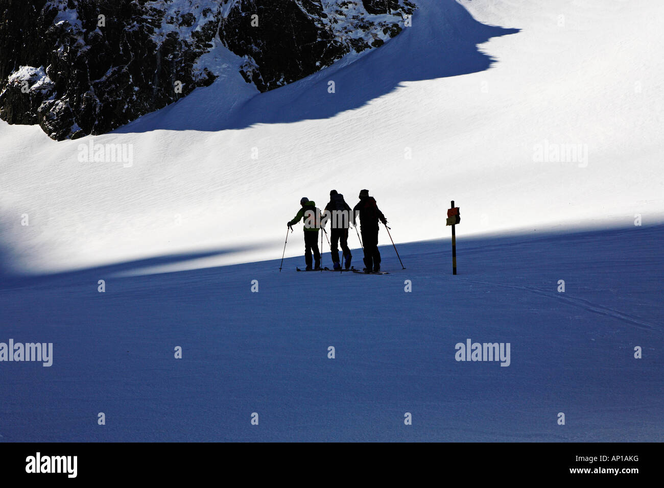 Three people on a ski tour, ascending a mountain, passing a sign post. The ski tourists are on their way up to the top of Maljov Stock Photo
