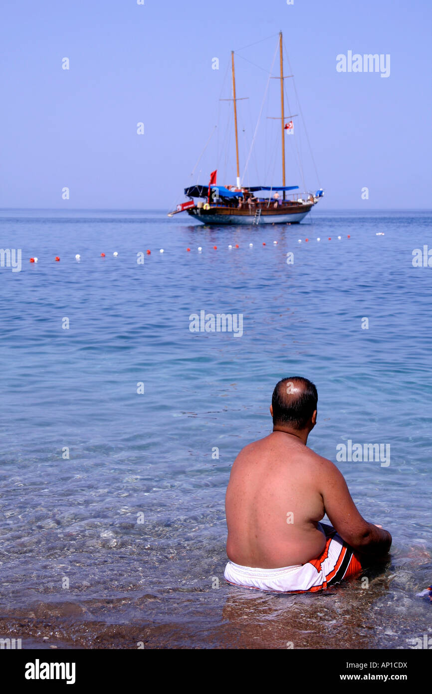 man sitting on pebble beach watching boat in distance Stock Photo - Alamy