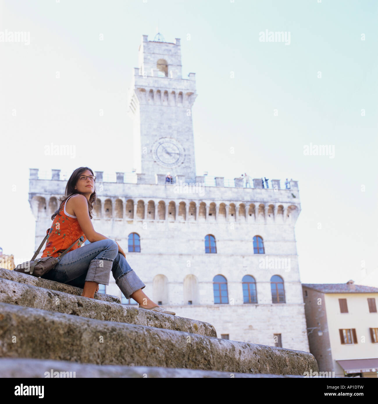 tourist in Montepulciano, Tuskany, Italy, portrait, female, woman sitting on steps, Piazza Grande, Palazzo Communale in the Back Stock Photo