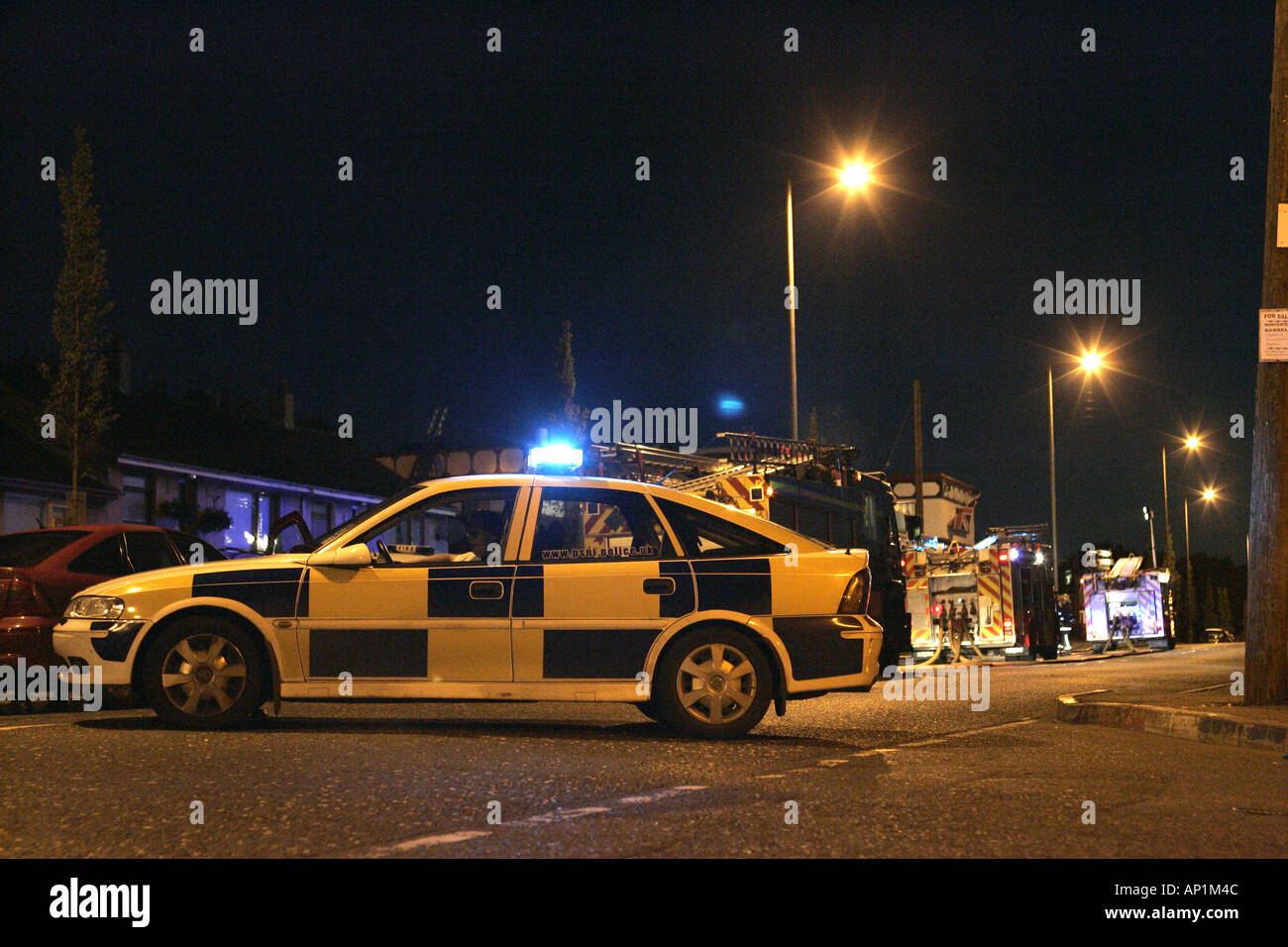 Police squad car and fire service vehicles attend fire at Cloughfern arms during loyalist feud at night Stock Photo