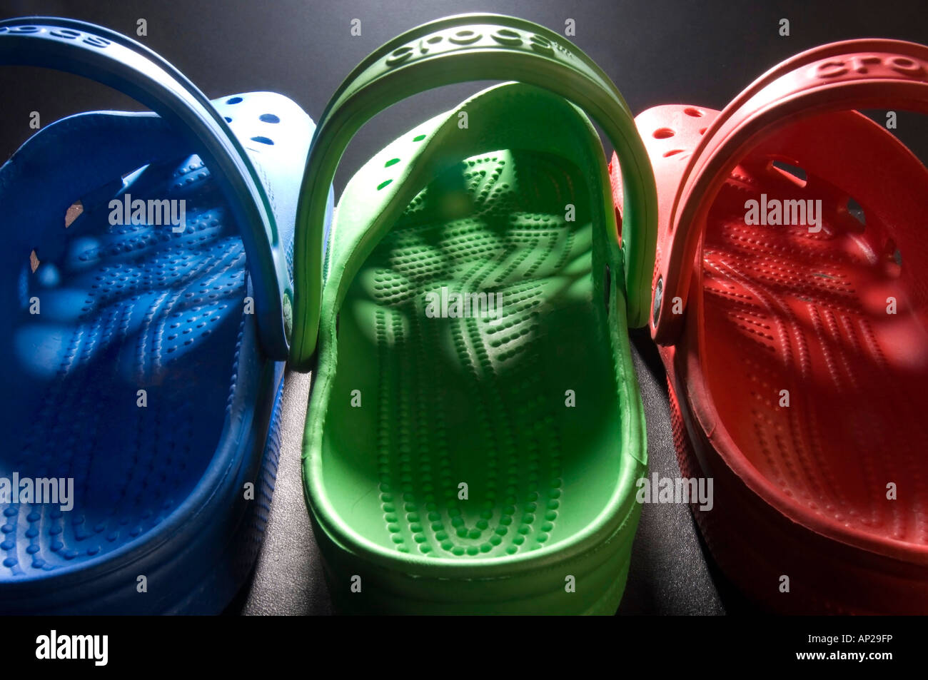 A row of  brightly coloured blue green and red Crocs clogs with light shining through the pattern of holes in the uppers Stock Photo