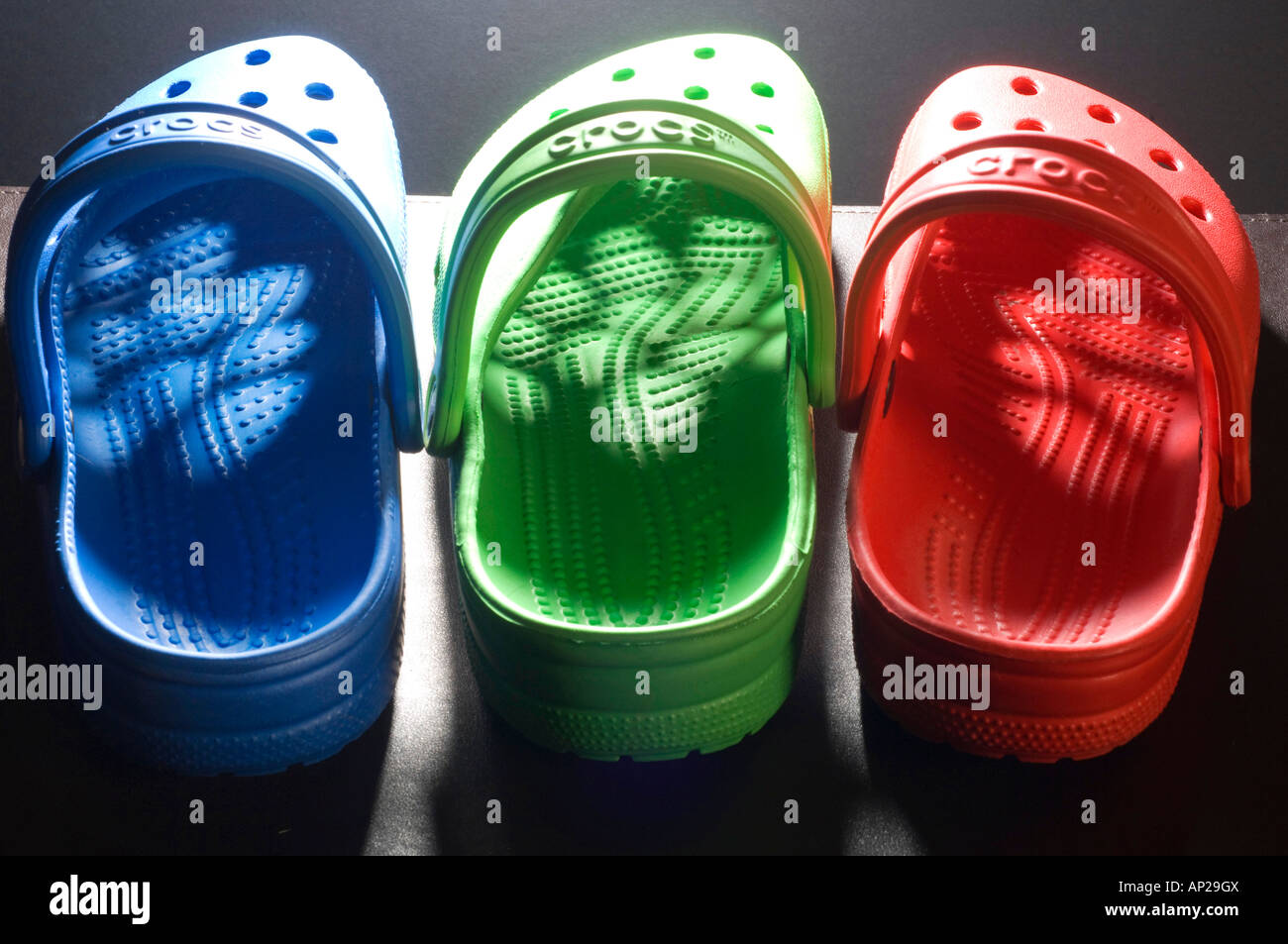 One blue one green one red Croc leisure shoes lined up in a row with light shining through the pattern of holes in the uppers Stock Photo