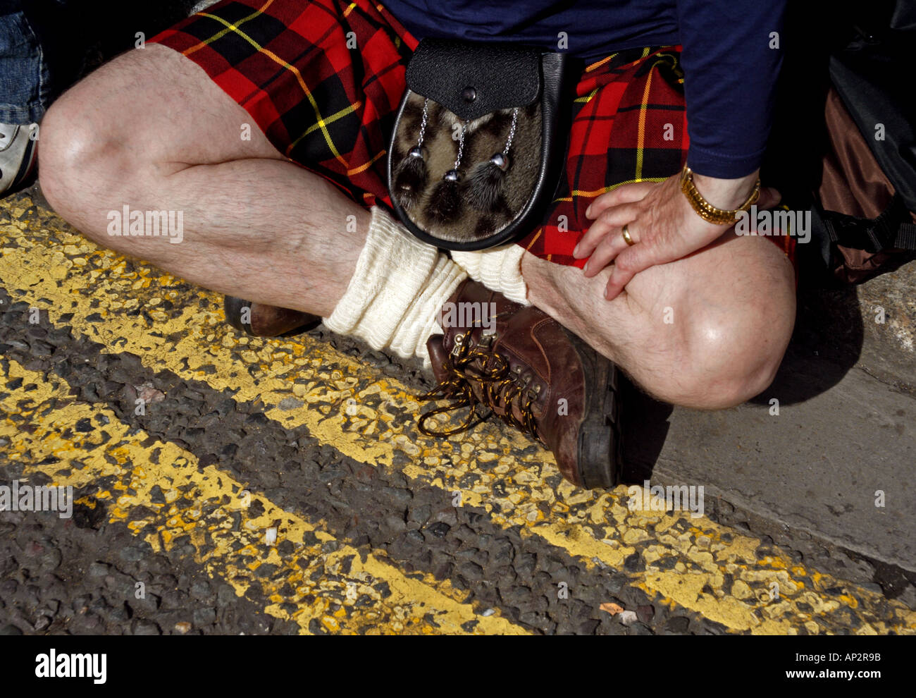 A scottish man in a kilt sits beside the road Stock Photo