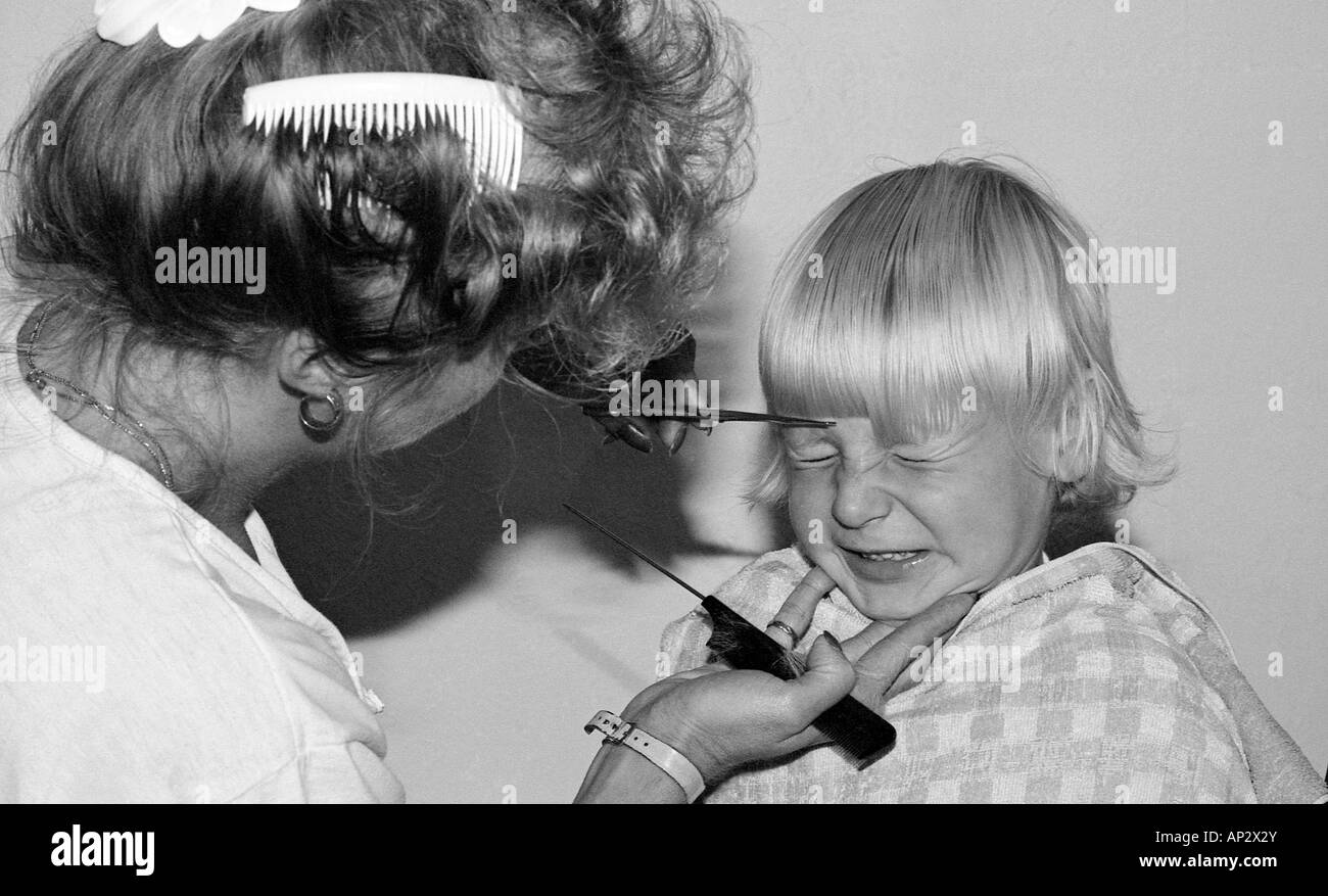 Young boy having his blonde hair fringe cut by a hairdresser and not liking it much. Stock Photo