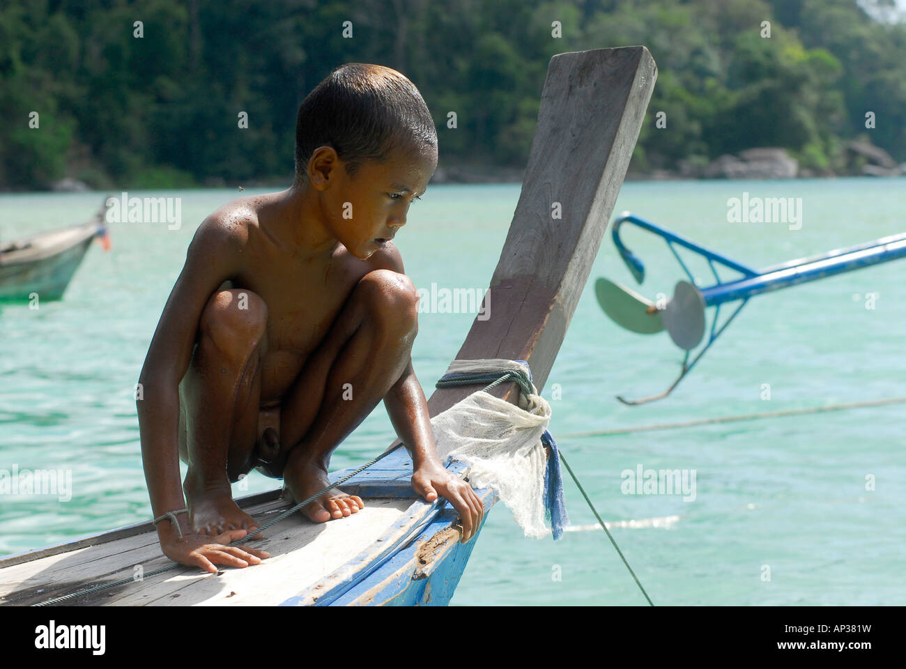 Child, boy, crouching on a boat, Chao Naam, Moken, Surin Islands Marine National Park, Ko Surin Noi, Phang Nga, Thailand Stock Photo