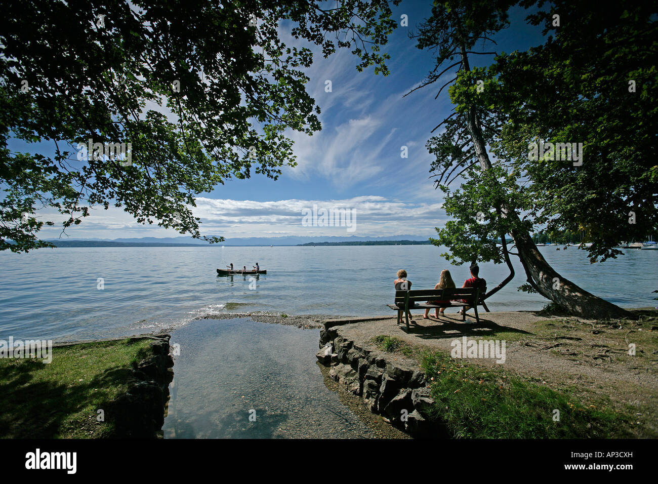 Three people sitting on the lakeshore, kanu in the background, Tutzing, Lake Starnberg, Bavaria, Germany Stock Photo