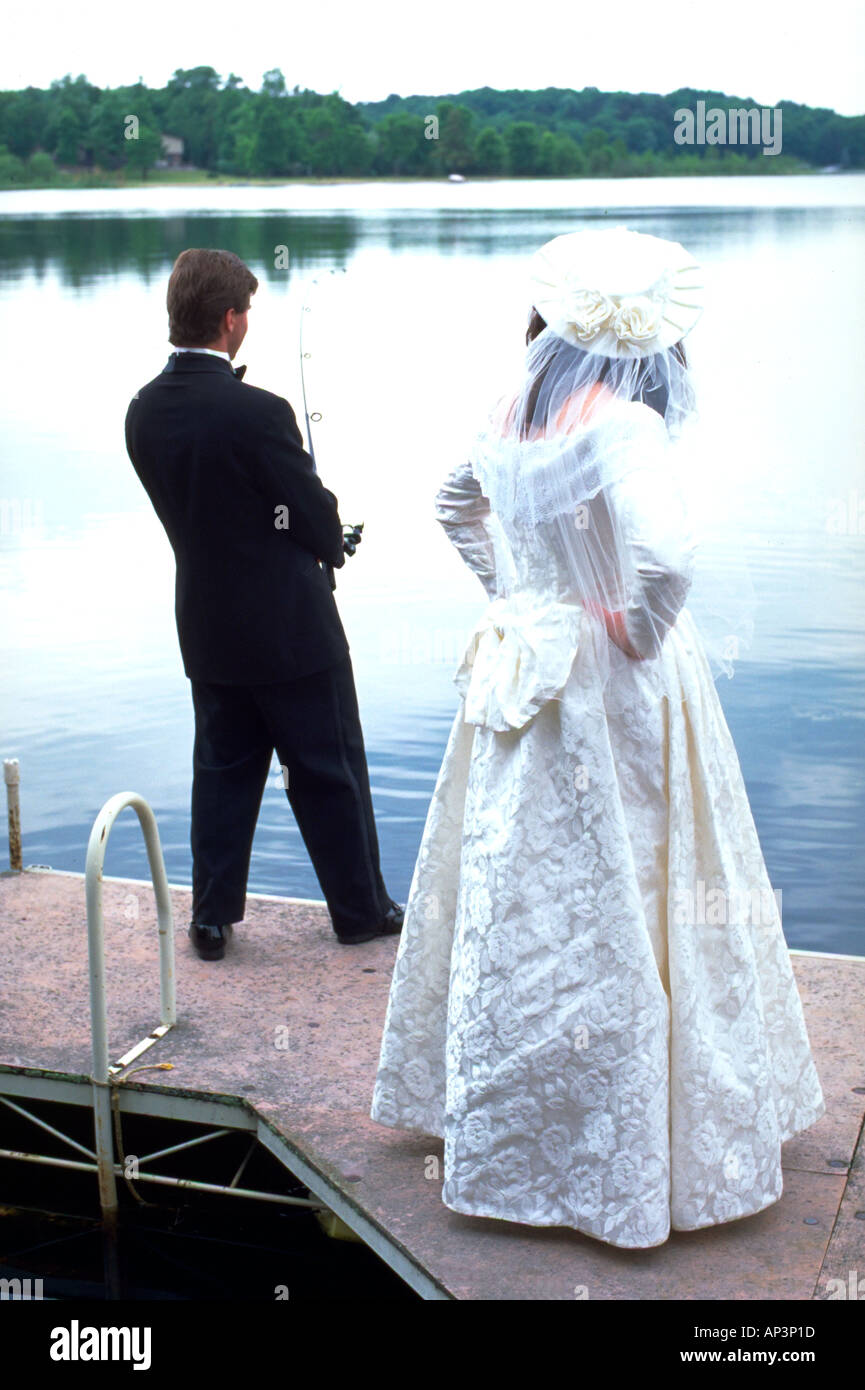 Groom fishing on dock as angry bride waits impatiently age 27. Roy Lake Nisswa Minnesota MN USA Stock Photo