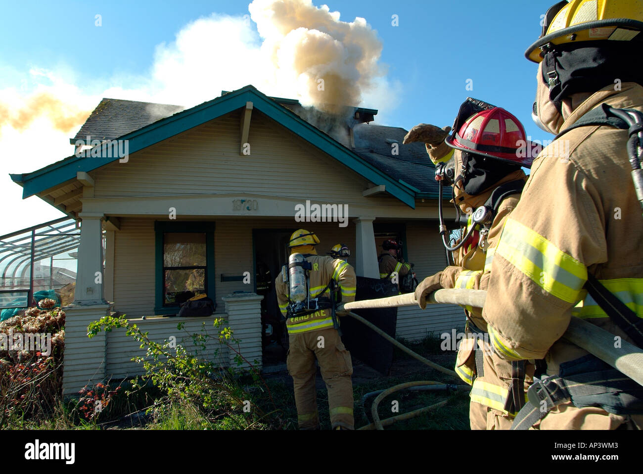 Smoke billows from a house as firefighters move in to attack the fire ...