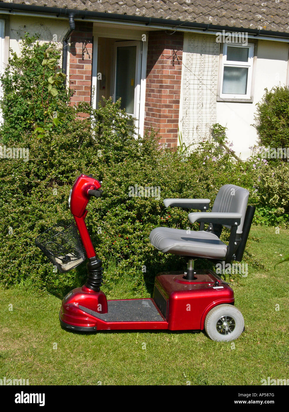 Three wheel electric wheel chair parked on lawn outside small bungalow in Bromham Wiltshire England UK EU Stock Photo