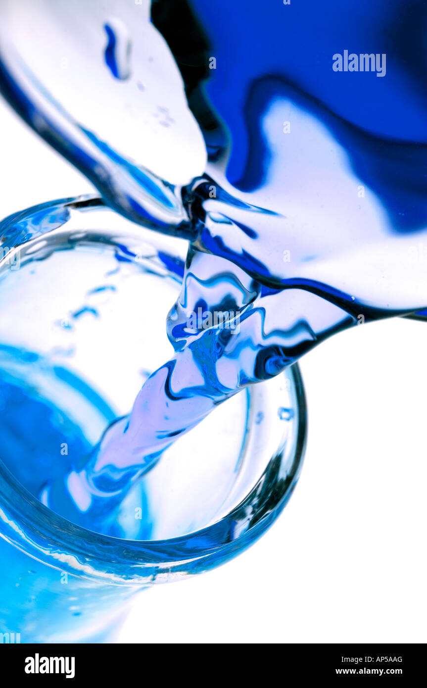 Blue colored liquid pouring from beaker into laboratory glass flask. Stock Photo