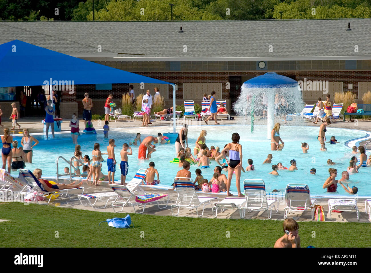 Adults and children swim and sunbathe at a public swimming pool in