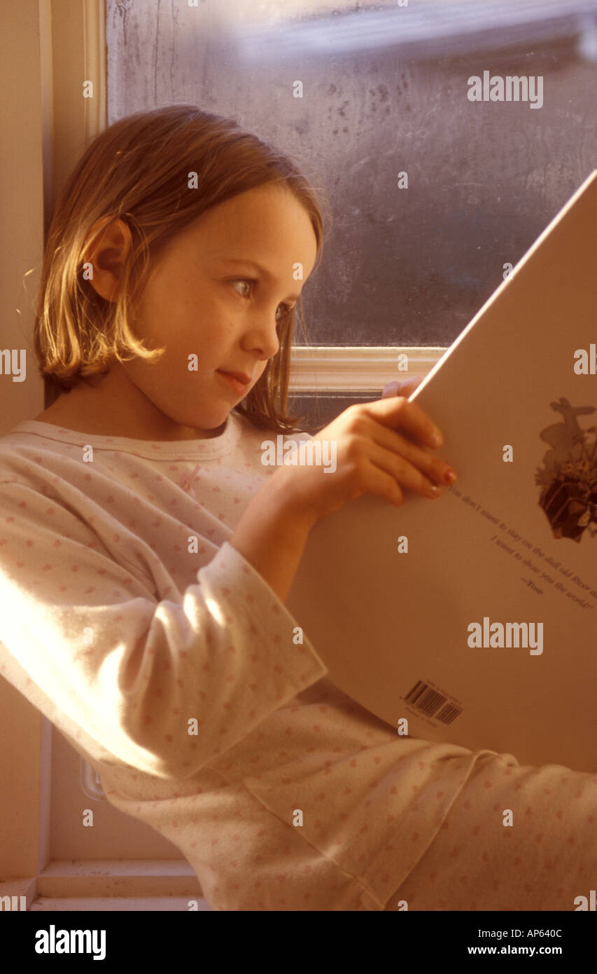 child reading a book in the window light Stock Photo