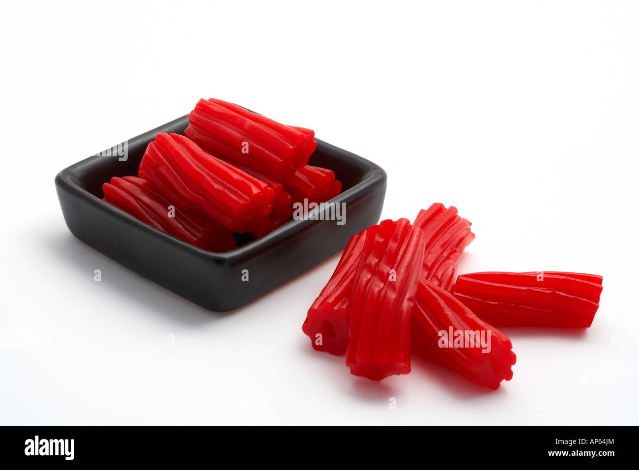 Pieces of red licorice on black bowl Isolated on white background Stock