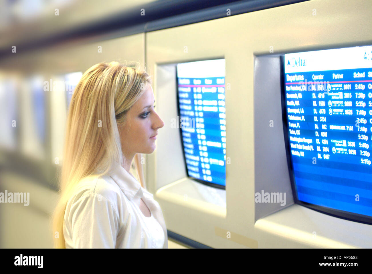 young businesswoman viewing flight schedule information on monitors at airport Stock Photo