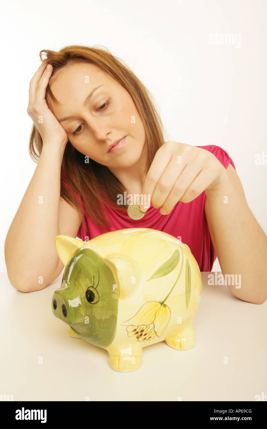 Sad young woman putting a pound coin into a piggy bank Stock Photo - Alamy