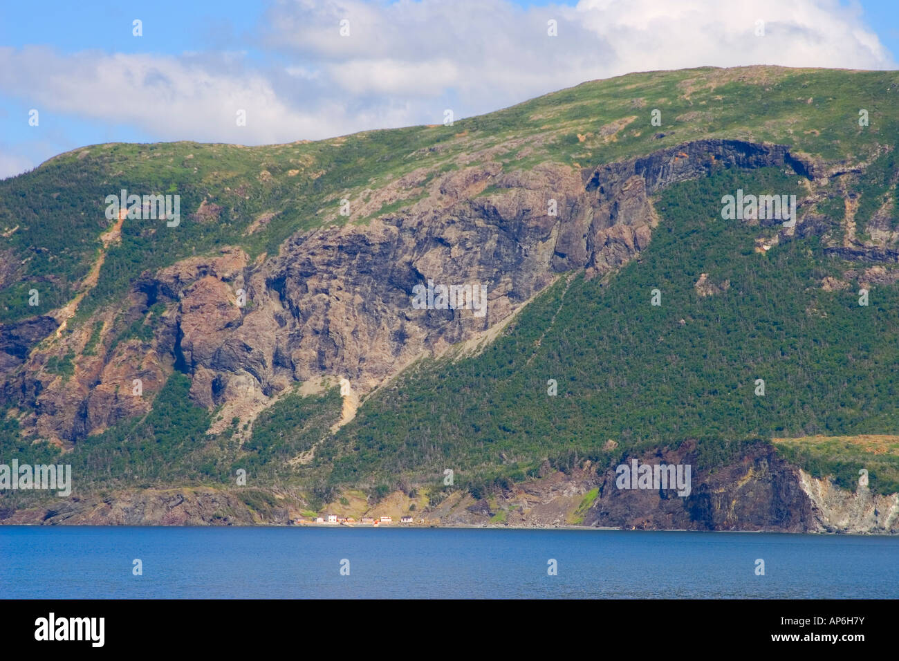Towering cliffs dwarf a small outport village on the Bay of Islands Newfoundland Stock Photo