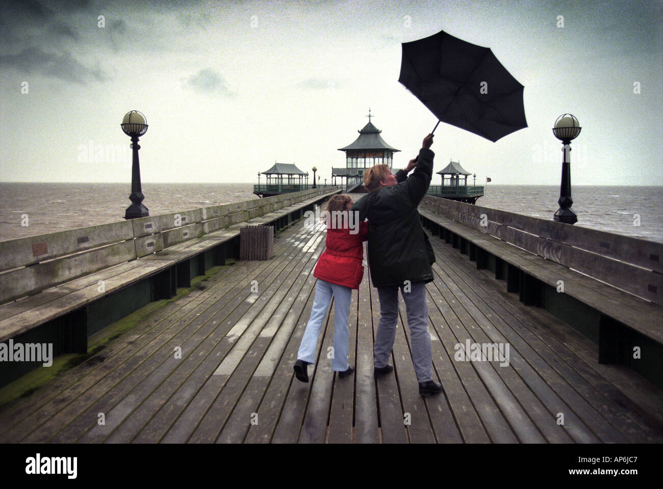 A GIRL AND HER MOTHER STRUGGLE WITH A BLACK UMBRELLA DURING A WALK ON CLEVEDON PIER NORTH SOMERSET UK Stock Photo