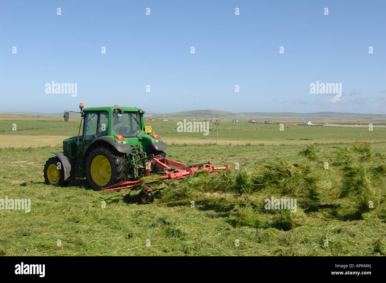 Tractor turning grass for hay making in field on Mainland Orkney Island