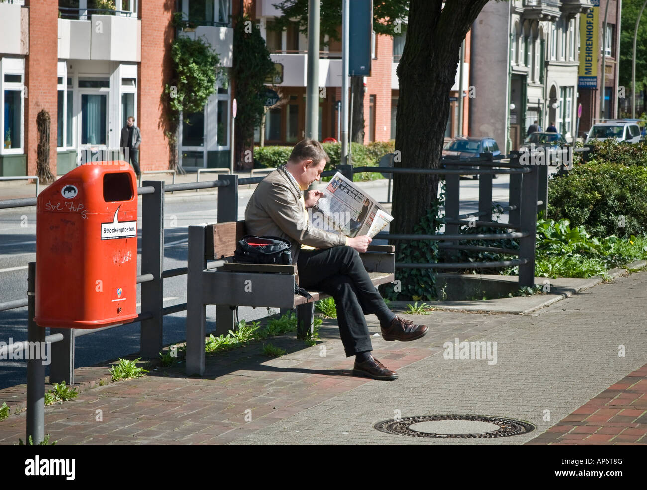 Man reading newspaper on a park bench Stock Photo - Alamy