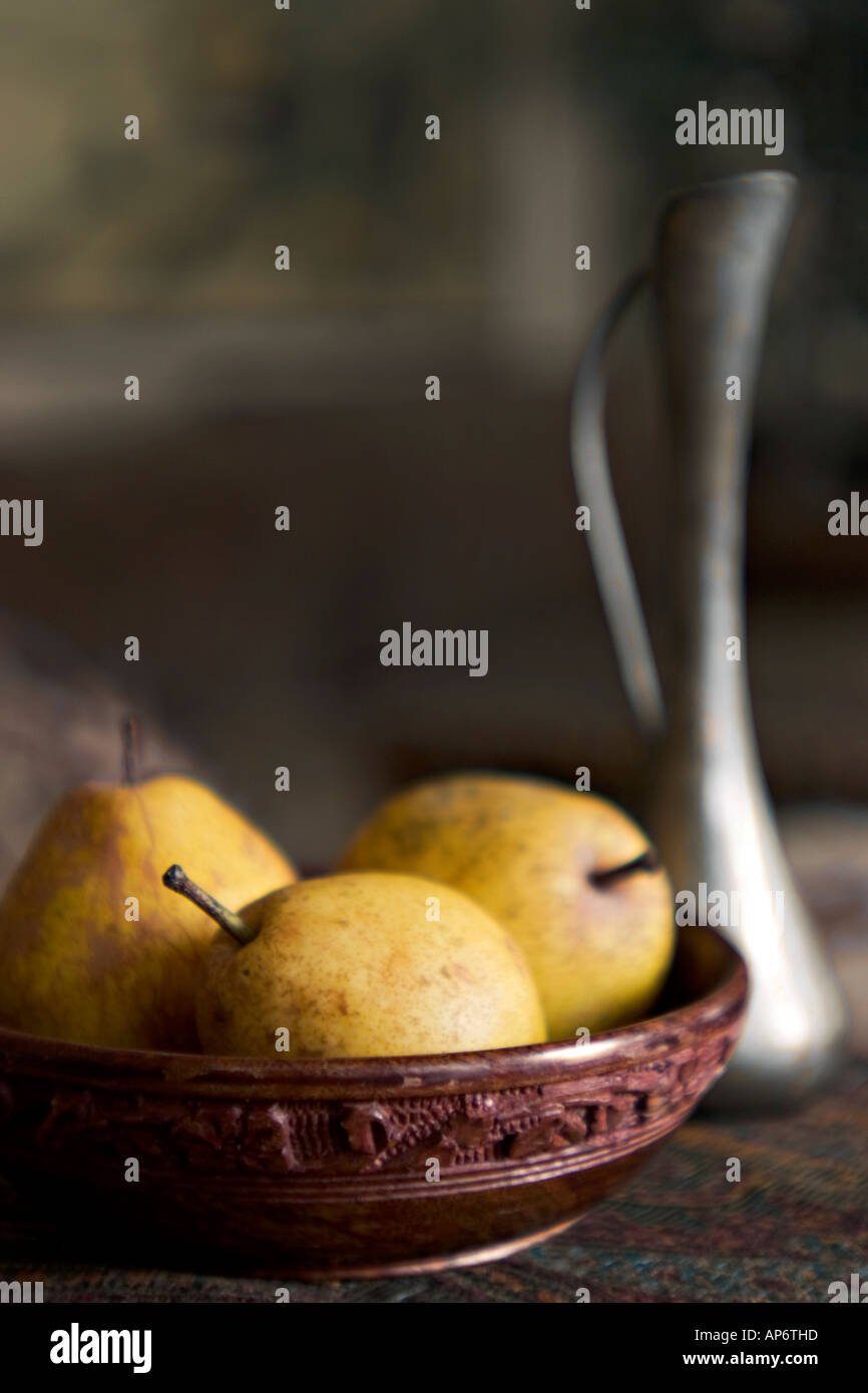 three pears in a wooden bowl with a pewter vase Stock Photo