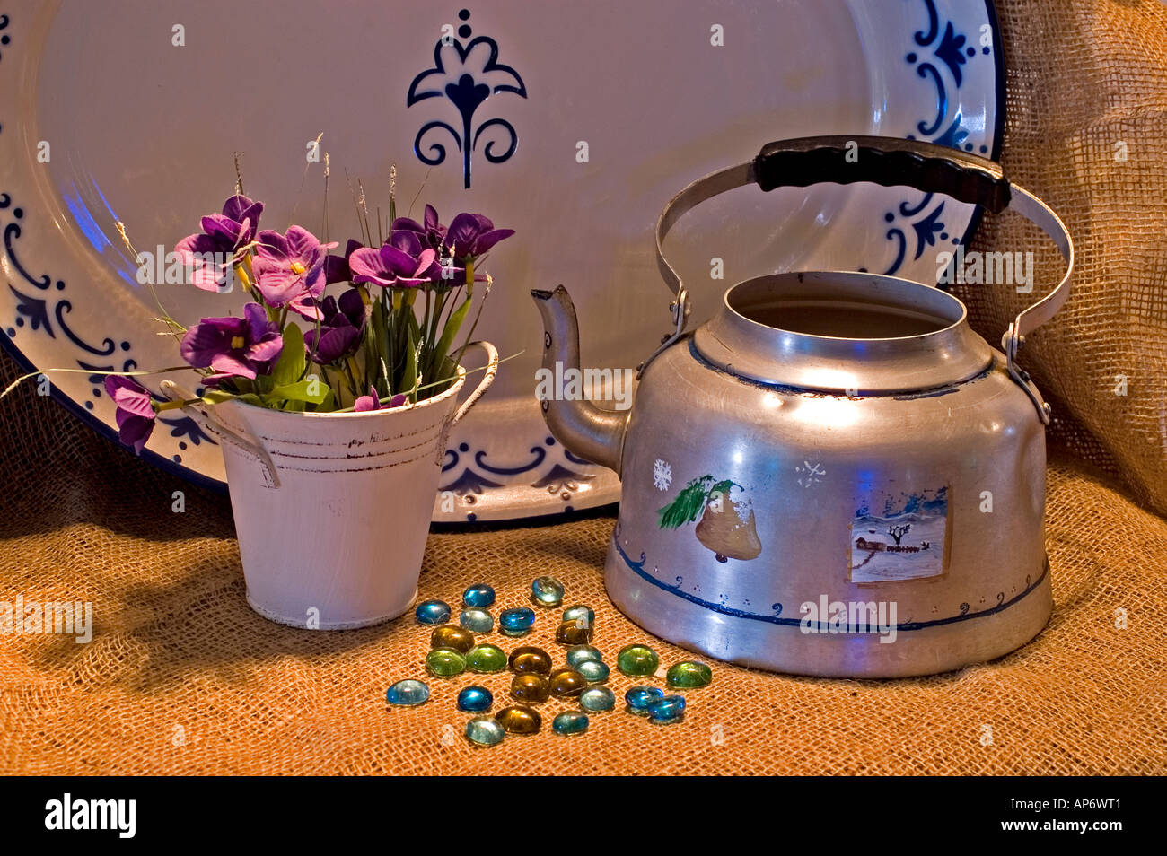 Still life with tin kettle and mauve flowers on a jute background Stock Photo