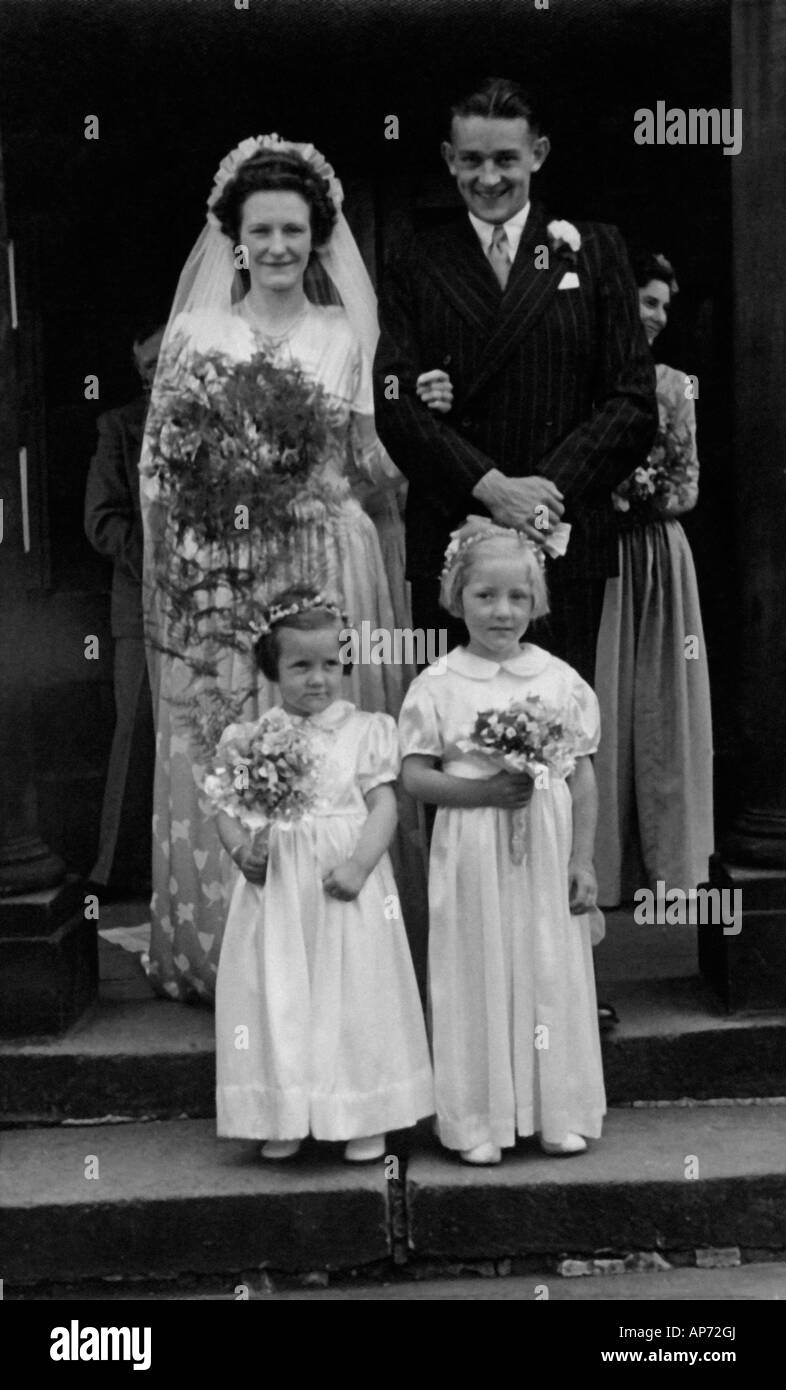 OLD BLACK AND WHITE FAMILY PHOTOGRAPH SNAP SHOT PORTRAIT OF BRIDGE AND GROOM STANDING WITH TWO BRIDES MAIDS CIRCA 1950 Stock Photo