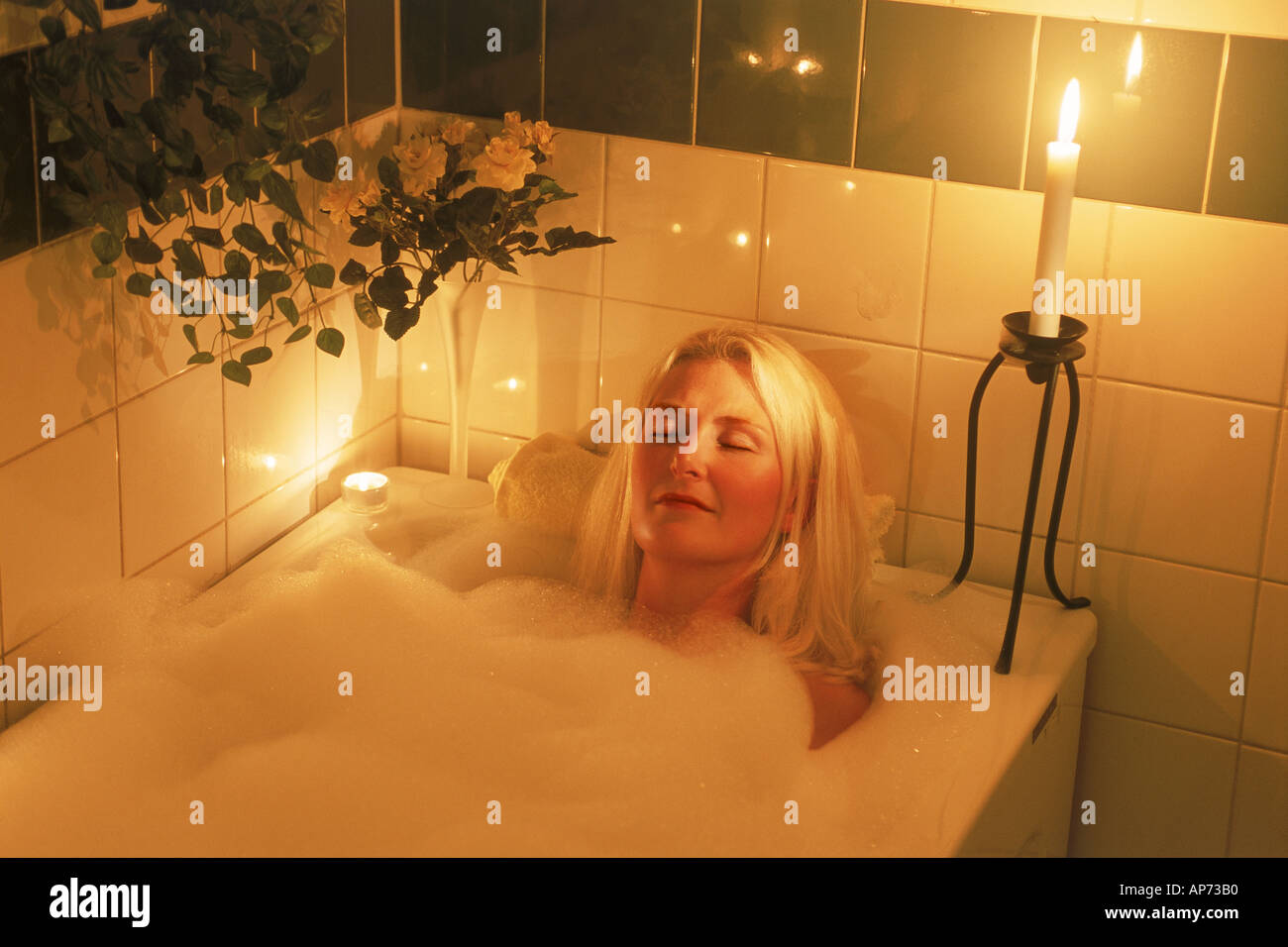Women soaking in bathtub with bubbles and candles Stock Photo