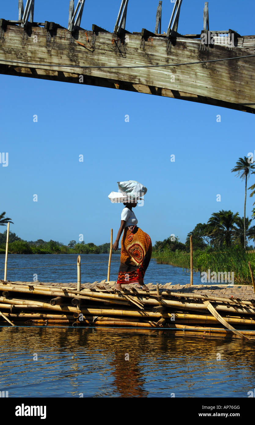 Pregnant woman with bag on head crosses makeshift bridge over the Pangalanes, Eastern Madagascar Stock Photo