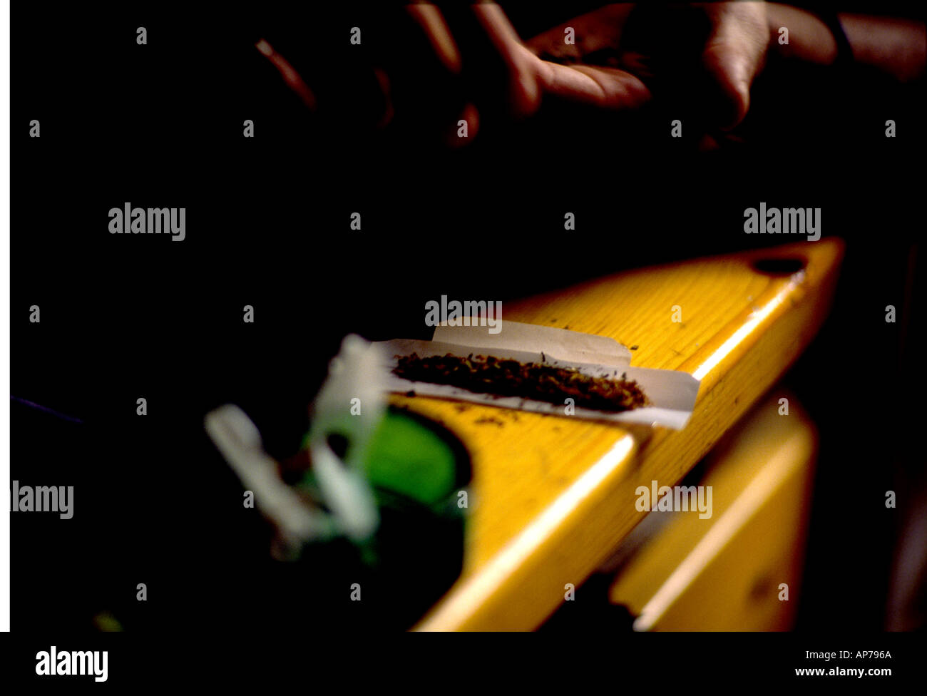 Joint with tobacco & cigarette rolling papers, being rolled on arm of chair. Stock Photo