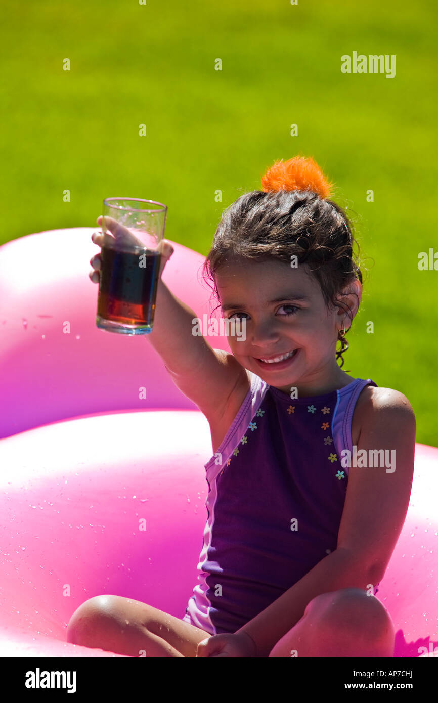 4 years old girl drinking mate at a picnic seated on an inflated pillow back lounge on the grass Stock Photo