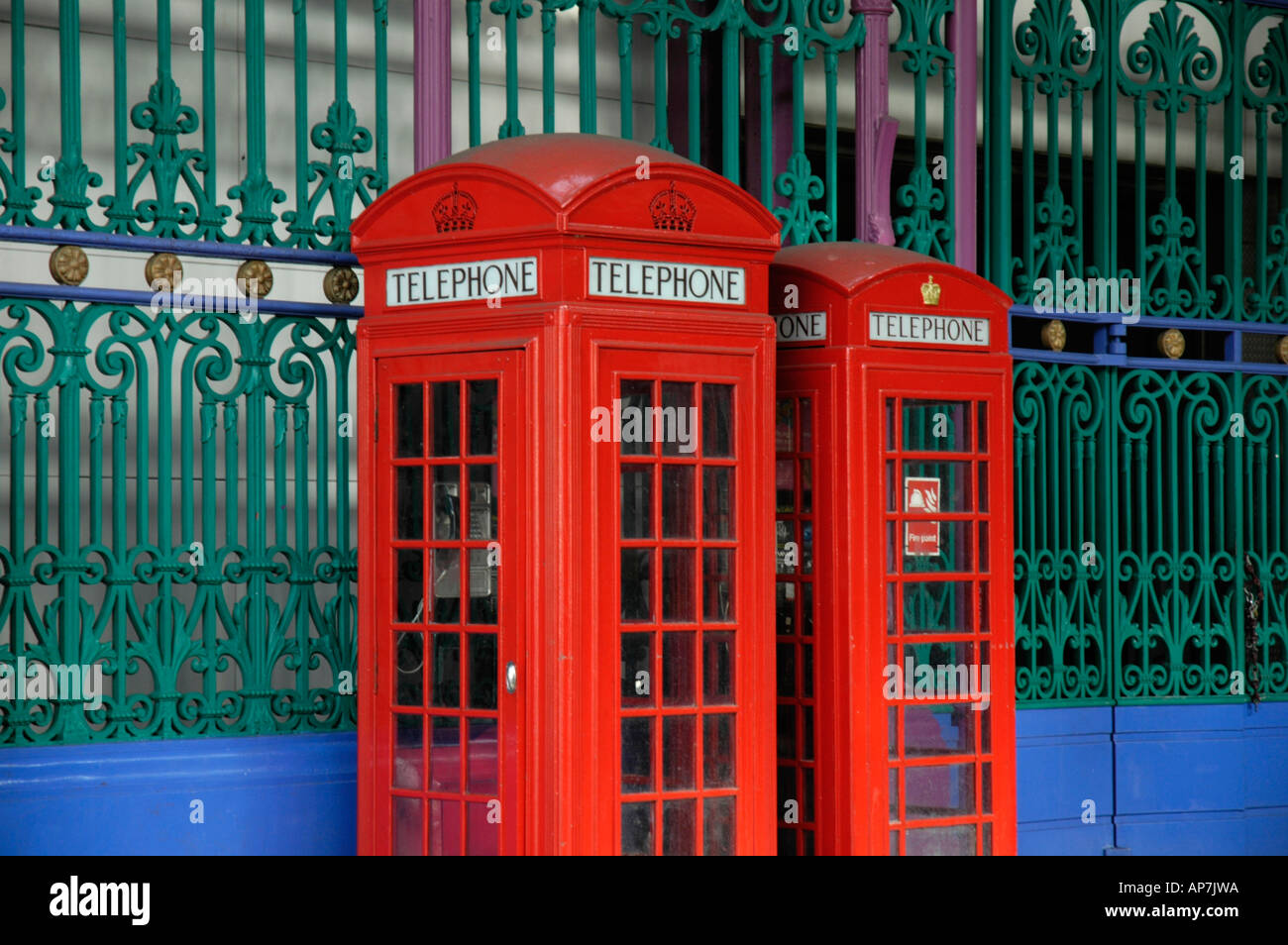 Two traditional British red telephone boxes against colourful Victorian ironwork, London, England, UK Stock Photo