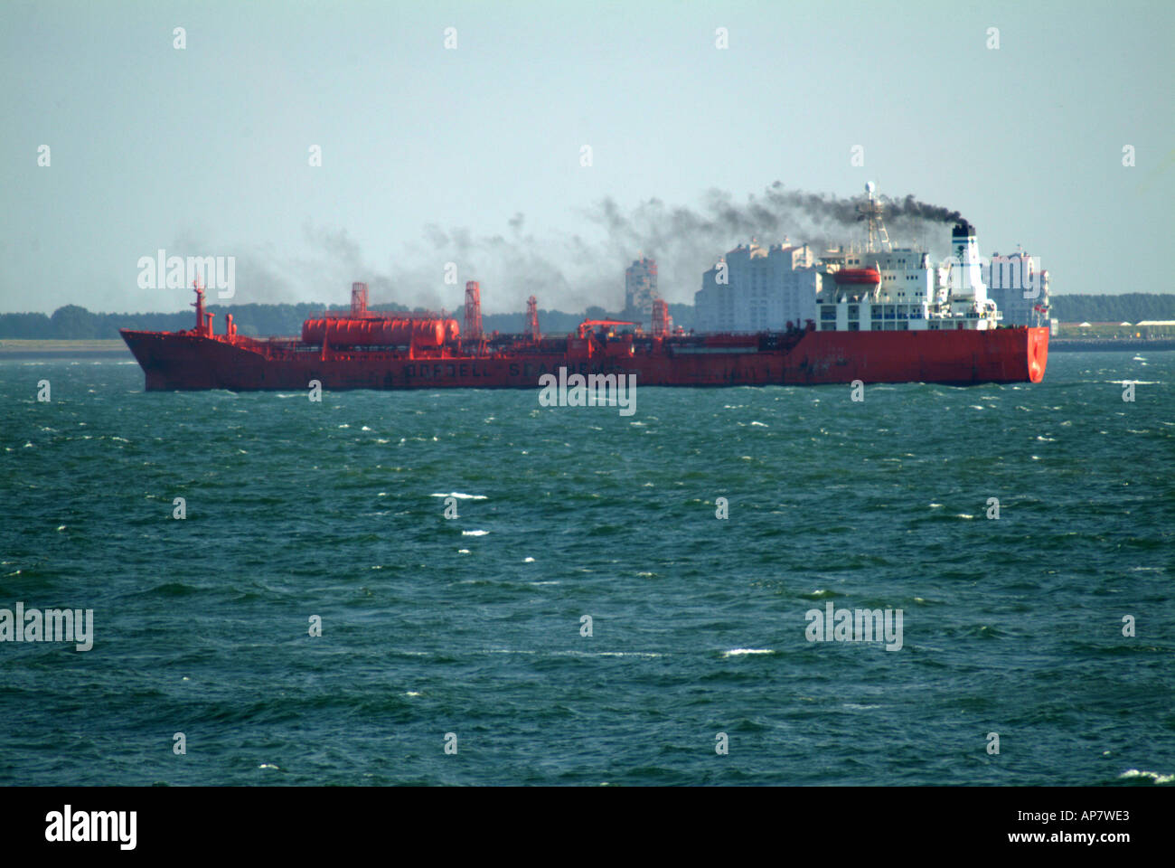 red cargo ship in estuary river smoke stack close to land Stock Photo