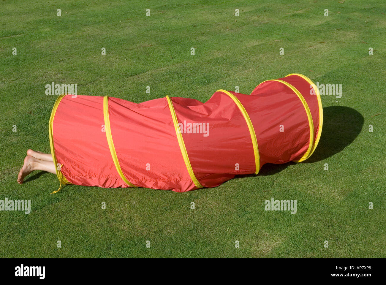 red play tunnel on grass lawn with child's feet sticking out Stock Photo