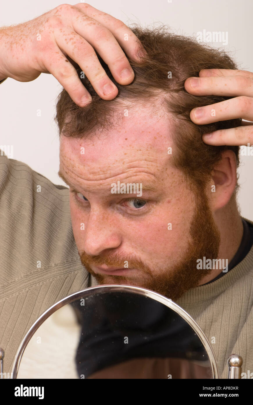 worried man looking in a mirror examining receding hairline worried he is going bald Stock Photo