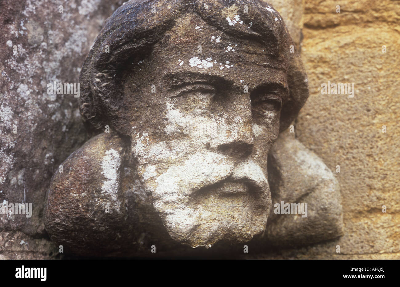 Close up of weathered carved sandstone head and shoulders of bearded man with lichen as corbel to stone arch Stock Photo