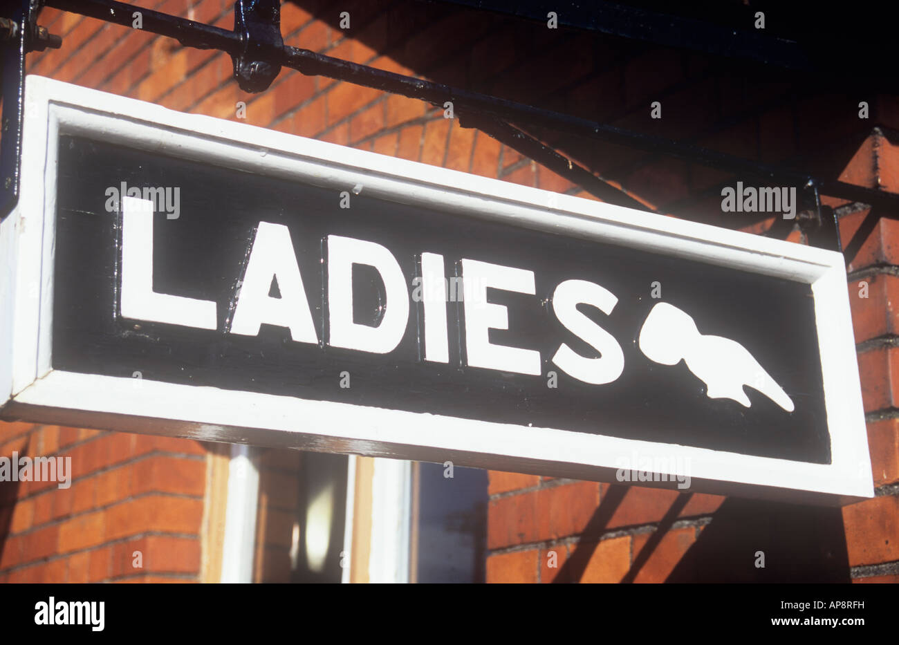 Old-fashioned carved wooden sign in black and white hanging from orange brick wall with pointing hand stating Ladies Stock Photo