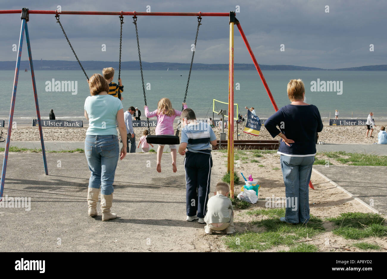 children and parents playing on swings and see saw at park at