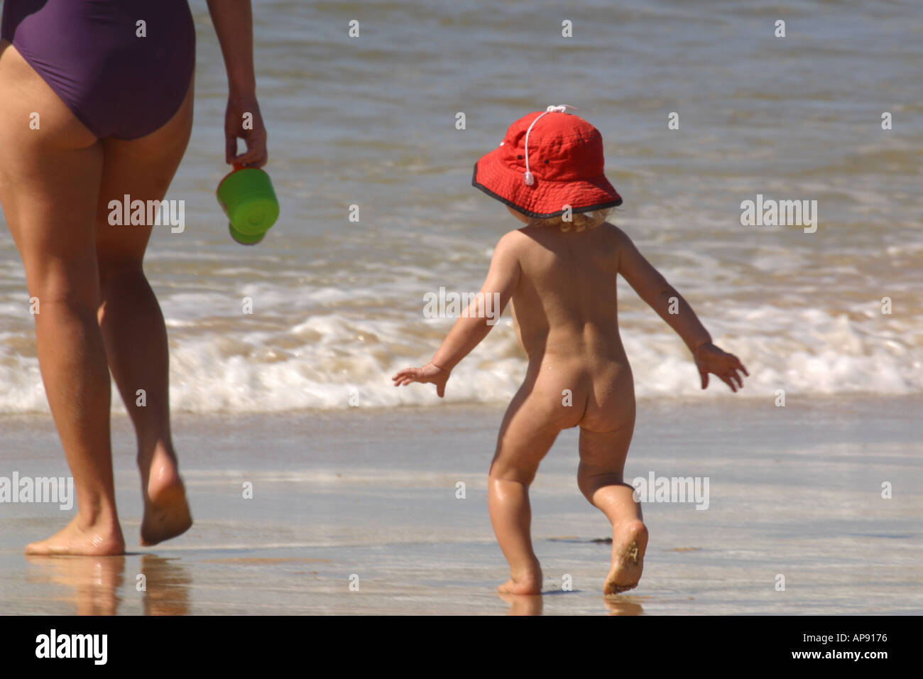 Baby running naked behind Mother on beach Stock Photo