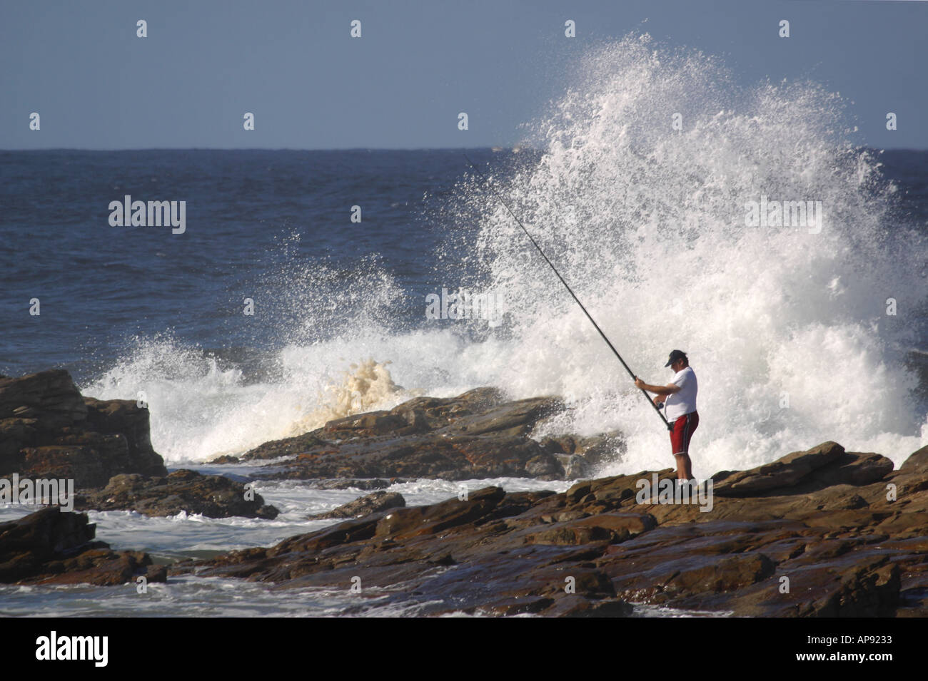 Fisherman surf fishing off rocky shore with waves breaking Stock Photo