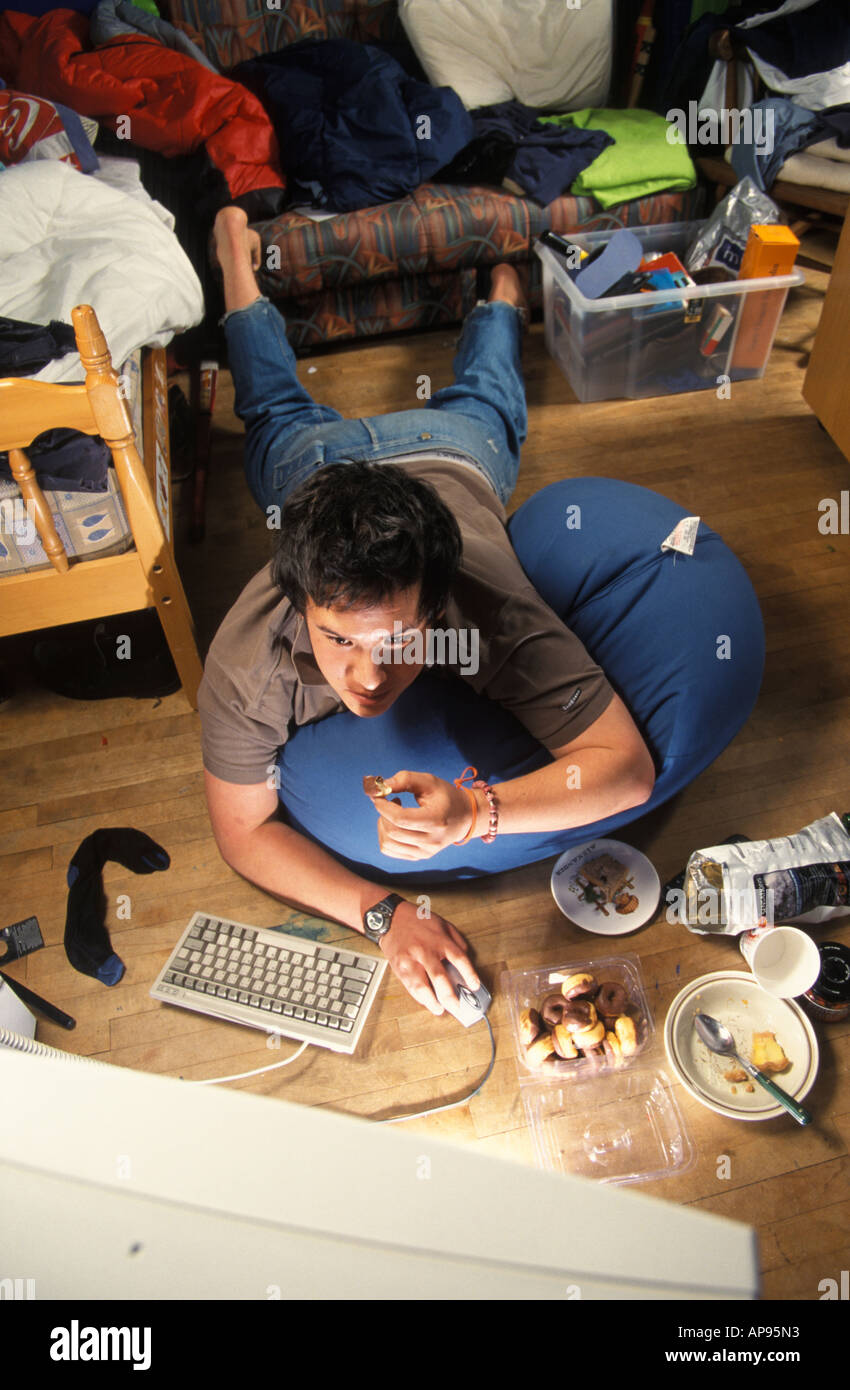 teenage boy on computer in untidy room snacking on junk foods Stock Photo