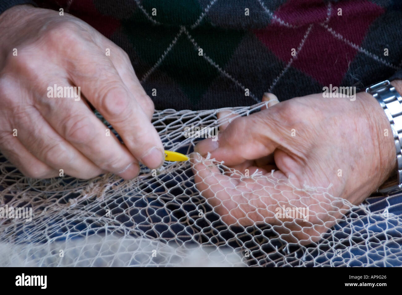 Elderly hands repairing a fishing net the old fashion way Stock