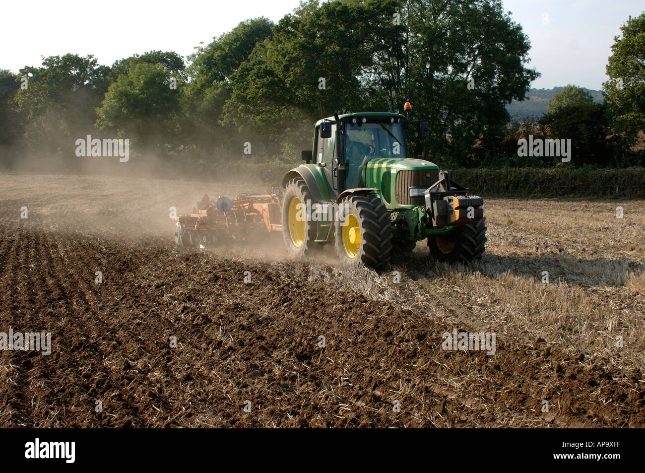 John Deere tractor power disc harrowing subsoiled stubble field before planting to barley Stock Photo