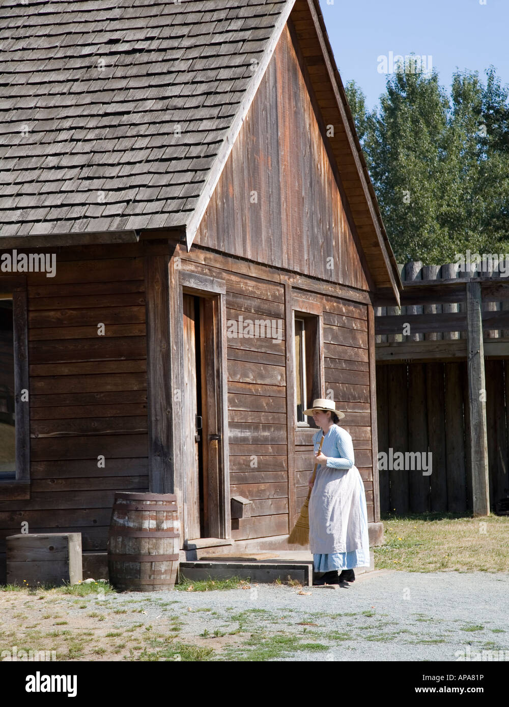 Woman in period costume sweeping steps outside wooden cabin Fort Langley British Columbia Canada Stock Photo