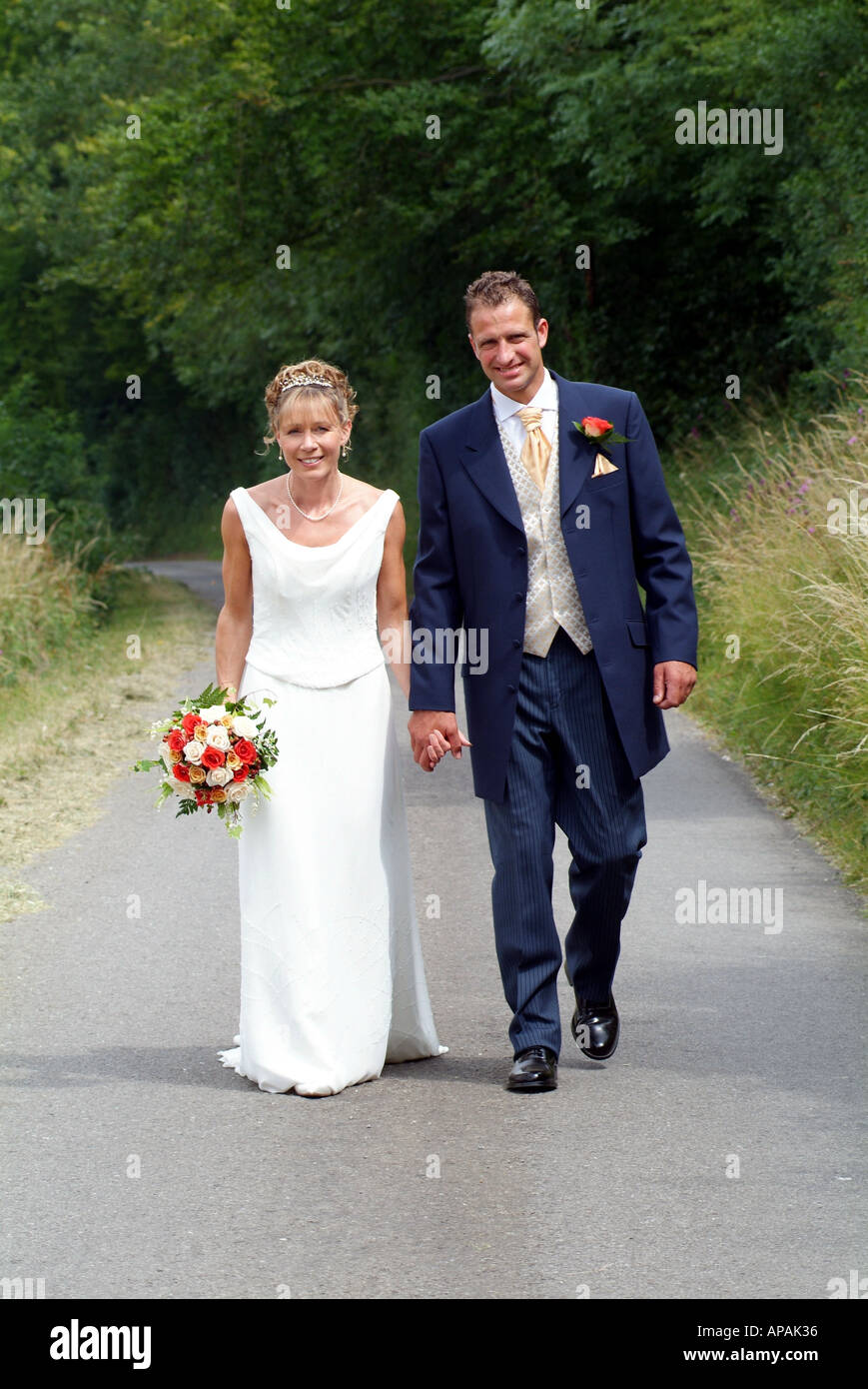 Bride And Groom Hold Hands Walking Along Country Lane Southern