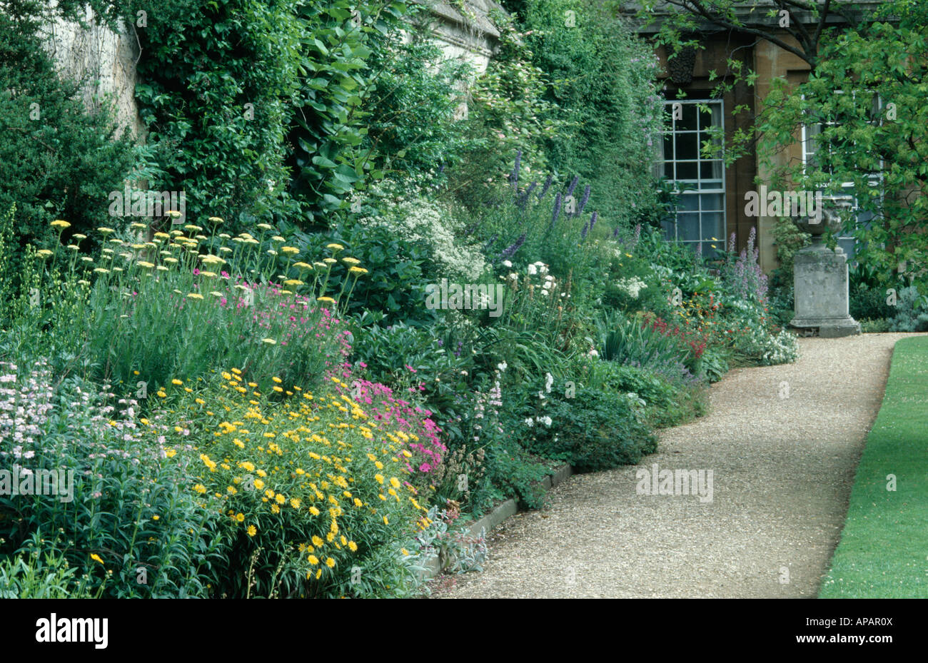 Yellow and pink summer flowering plants in herbaceous border beside gravel path in Oxford Botanic Garden Stock Photo
